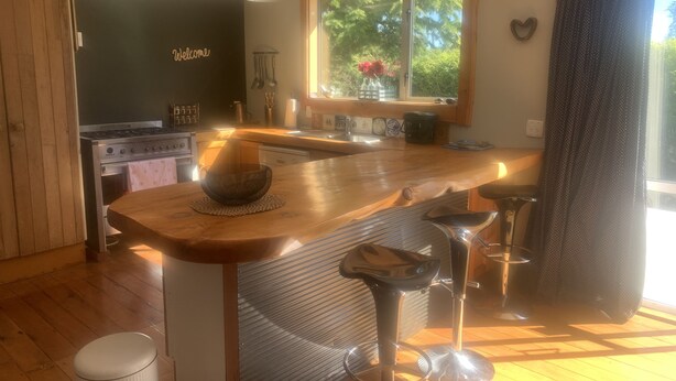A modern kitchen with a wooden island, bar stools, a stove, and a window with a view of greenery.