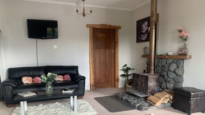 A living room with a black leather sofa, a fireplace, a stone wall, and a television mounted on the wall.