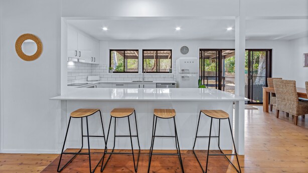 Una cocina moderna con una isla central, taburetes de bar y un comedor con sillas de mimbre.