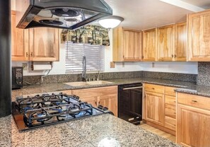 Kitchen features a gas stove, dishwasher, and wooden cabinets with a granite countertop and stainless steel range hood.