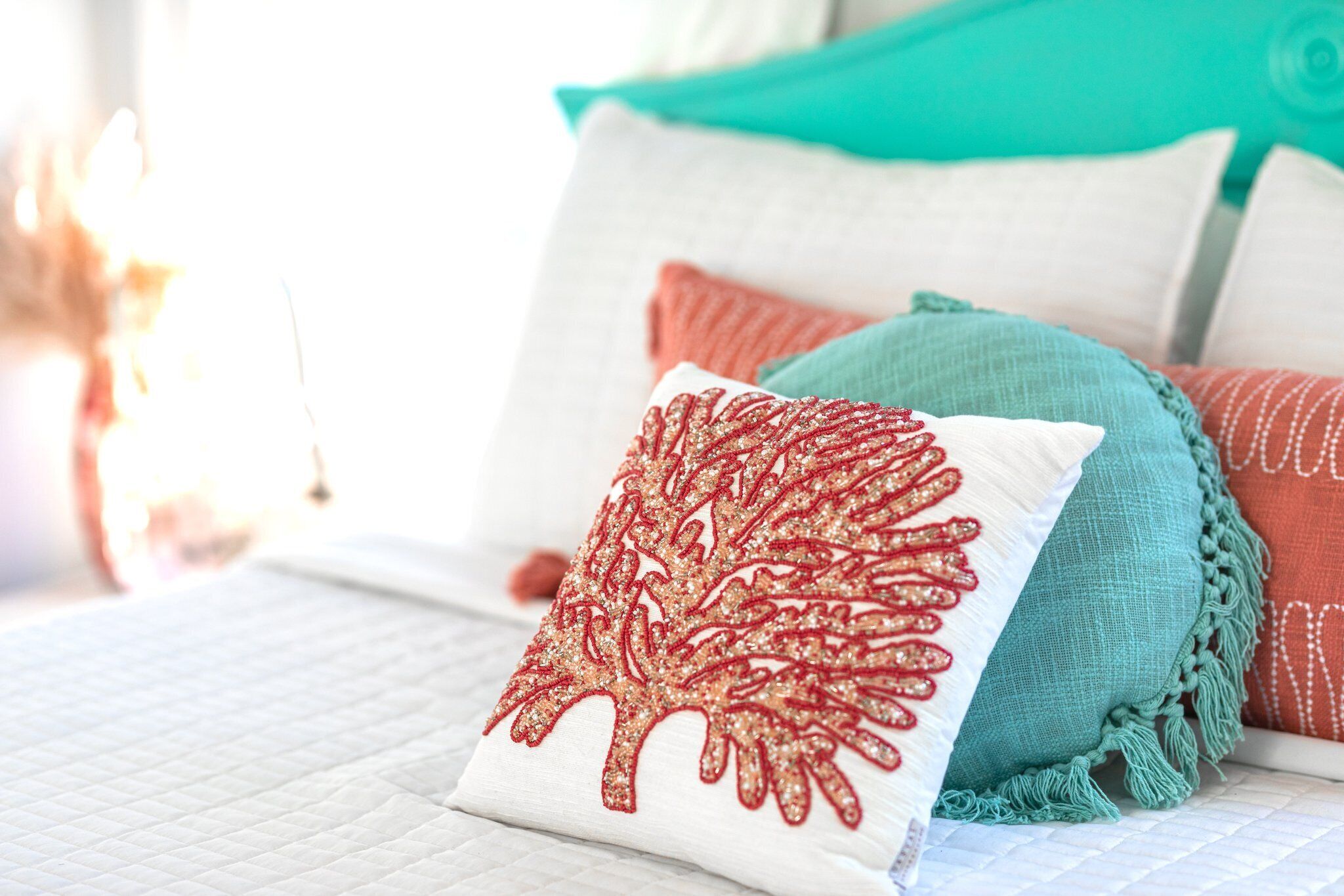 A neatly arranged bed with a quilted white bedspread, a decorative red pillow with a leaf pattern, and a teal throw blanket.