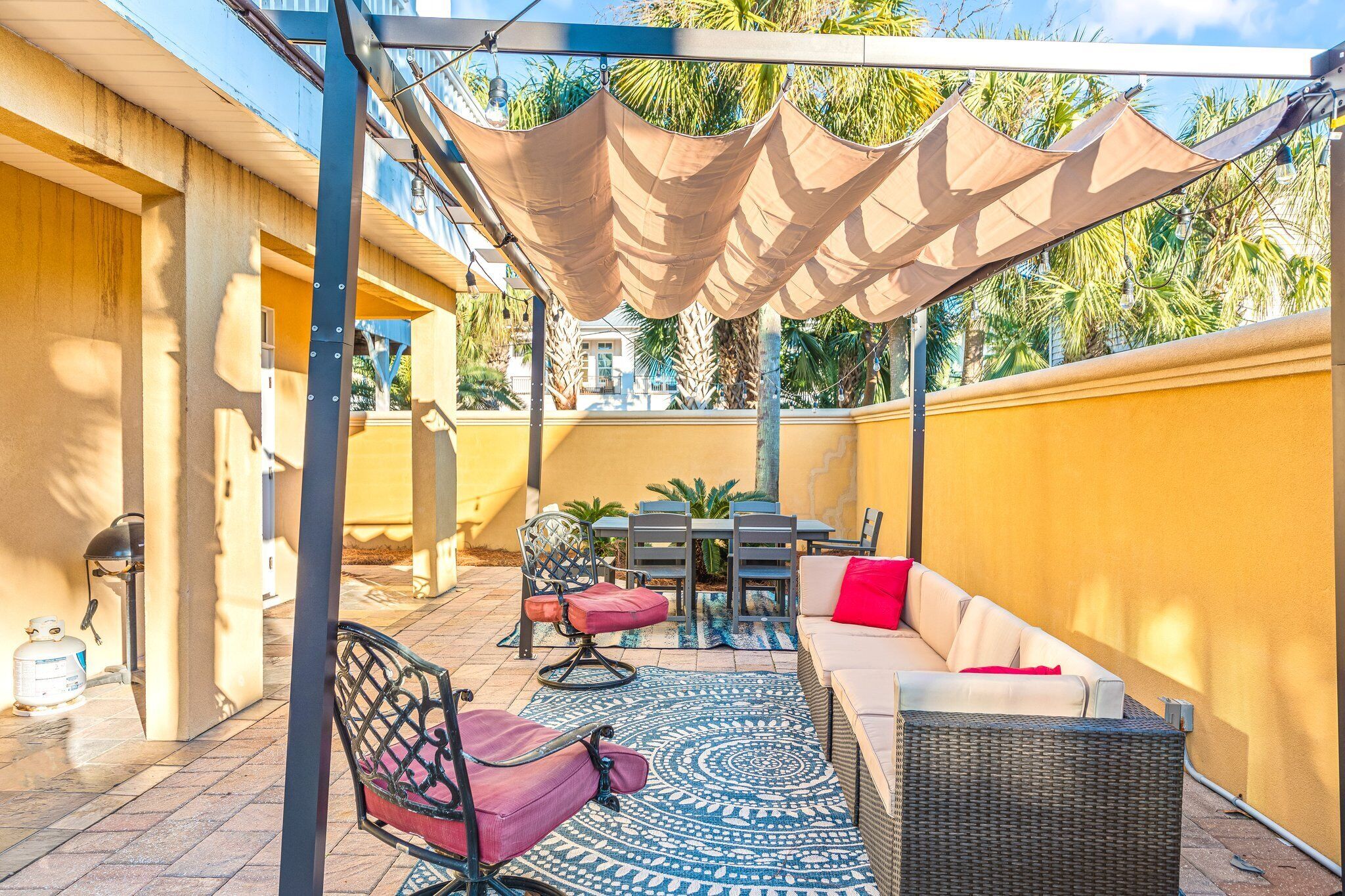 An outdoor patio with a dining table, chairs, a sofa, and a shaded area with a pergola.
