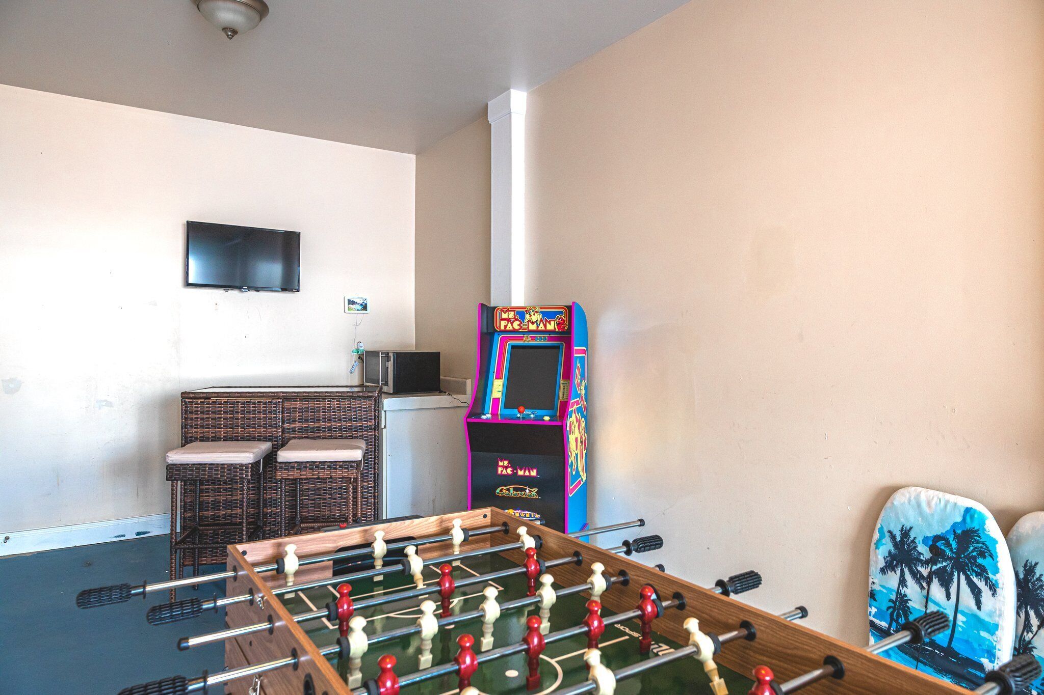 Una habitación con mesa de futbolín, máquina arcade de Pac-Man y muebles de mimbre.