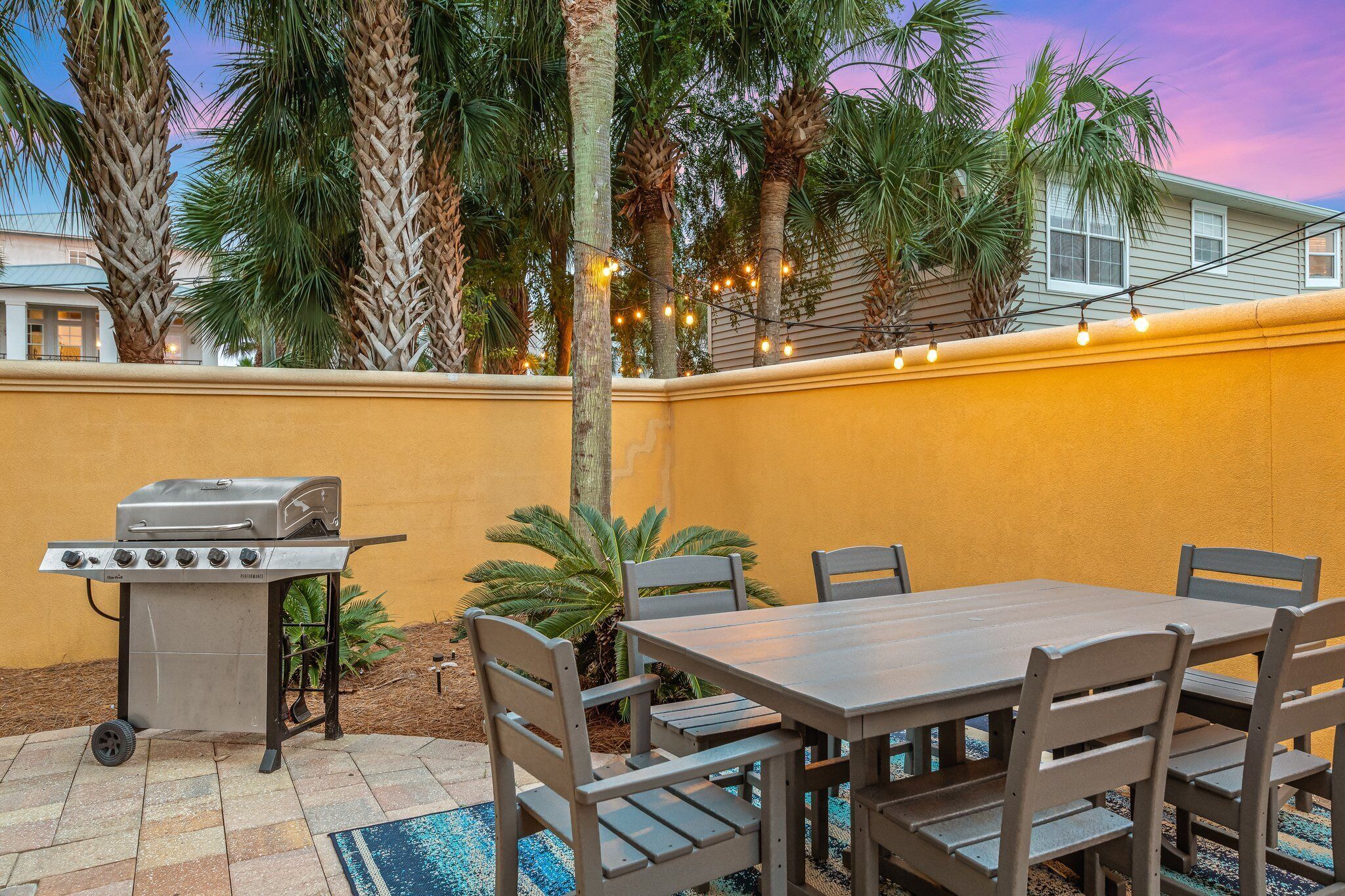 Un patio al aire libre con una parrilla, mesa de comedor, sillas y luces colgantes.