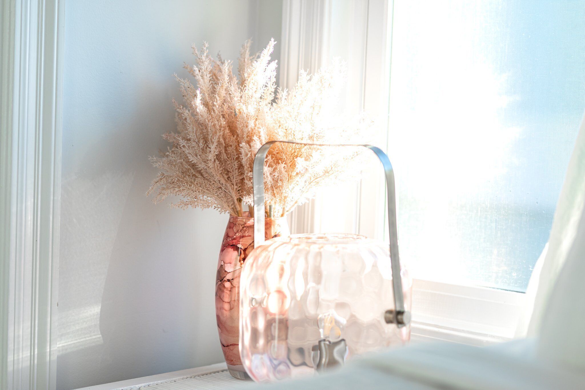 Un vase en verre transparent contenant des herbes de la pampa séchées, posé sur un rebord de fenêtre.