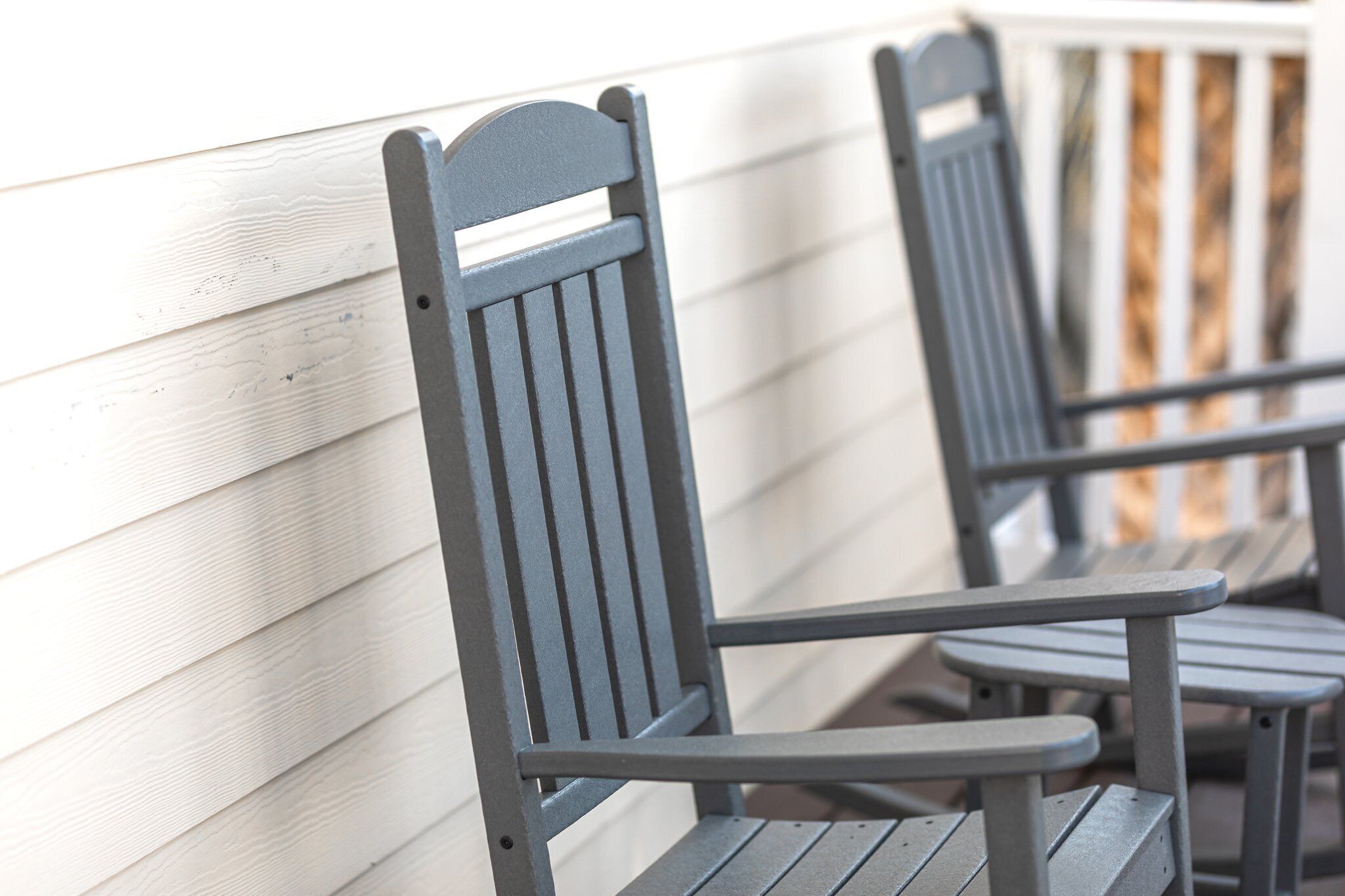 Two outdoor metal chairs with a slatted backrest and a flat seat, positioned against a white wooden wall.