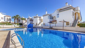 En swimmingpool med en klar, blå vandoverflade, omgivet af hvide bygninger med gule detaljer og en trappe, der fører til en balkon.