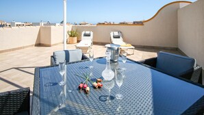 En tagterrasse med et glasbord, liggestole og udsigt over byens skyline.
