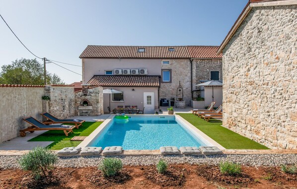 Una villa con piscina, muros de piedra y tejado de baldosas.