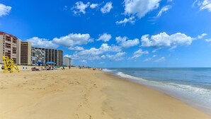 Une plage avec un hôtel en arrière-plan, caractérisée par une étendue de sable, un ciel bleu clair et des vagues de l’océan.