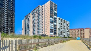 Un hôtel situé en bord de mer, composé de plusieurs immeubles de grande hauteur, doté d’une plage de sable et d’une clôture en bois.