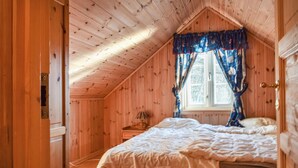 Ein gemütliches Schlafzimmer mit schrägen Wänden, einem Einzelbett, einem Nachttisch und einem Fenster mit Vorhängen.