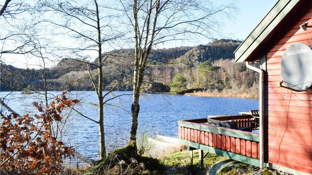 Eine Holzhütte mit einem Steg, der in einen See führt, umgeben von Bäumen und Hügeln.