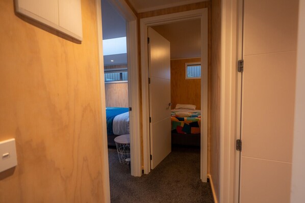 A narrow hallway leading to a bedroom with a bed, a small round table, and a window with blinds.