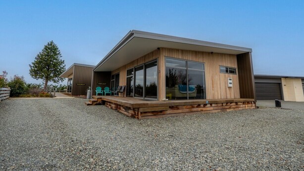 A modern house with a wooden deck, large sliding glass doors, and a small outdoor seating area with two chairs. - The Starlight Townhouse (Twizel)