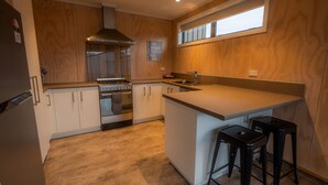 A modern kitchen with wooden cabinets, a built-in stove, and a large island with bar stools. - The Starlight Townhouse (Twizel)