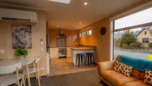 A modern kitchen with a central island, a dining area with a white table and chairs, and a cozy living room with a leather sofa and a large window. - The Starlight Townhouse (Twizel)