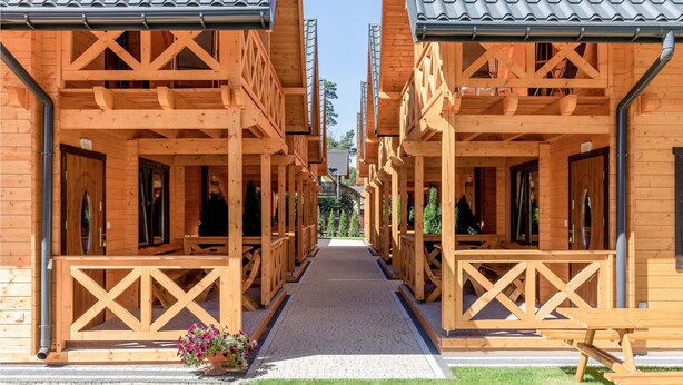 A row of wooden cabins with a central walkway, each featuring a balcony and a window. - Nice home in Pobierowo with WiFi (Pobierowo)