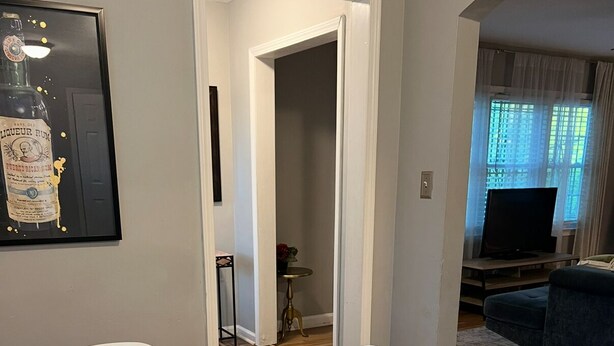 Un comedor con mesa de vidrio y sillas blancas, un cuadro en la pared y un televisor al fondo.