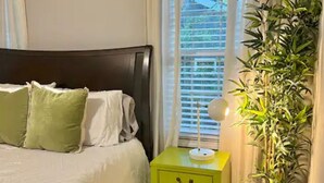 Un dormitorio con una cama, una mesita de noche verde, una lámpara de noche y una planta en maceta.