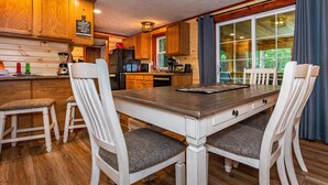 Una cocina de madera con comedor, que cuenta con una isla grande, sillas blancas y vistas a través del ventanal.