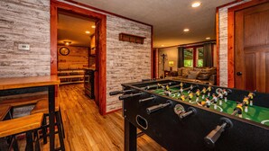Una habitación con mesa de fútbol de mesa, bancos de madera, una zona de bar y un rincón de estar acogedor con un sofá y una lámpara.