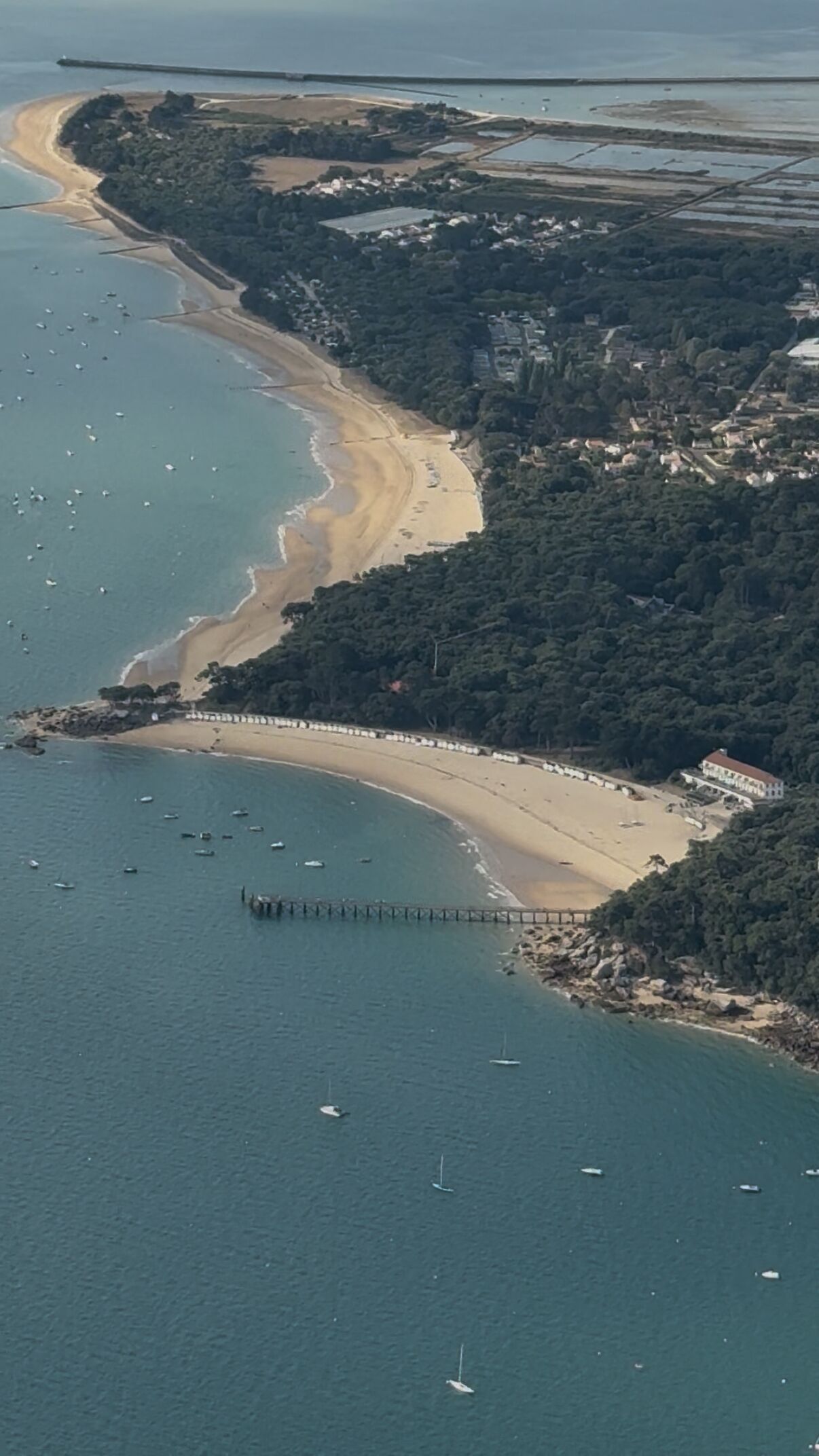 An aerial view of a coastal area with a beach, a pier, and boats.