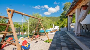 A children's play area with swings and slides, a pool, and a patio with outdoor seating.