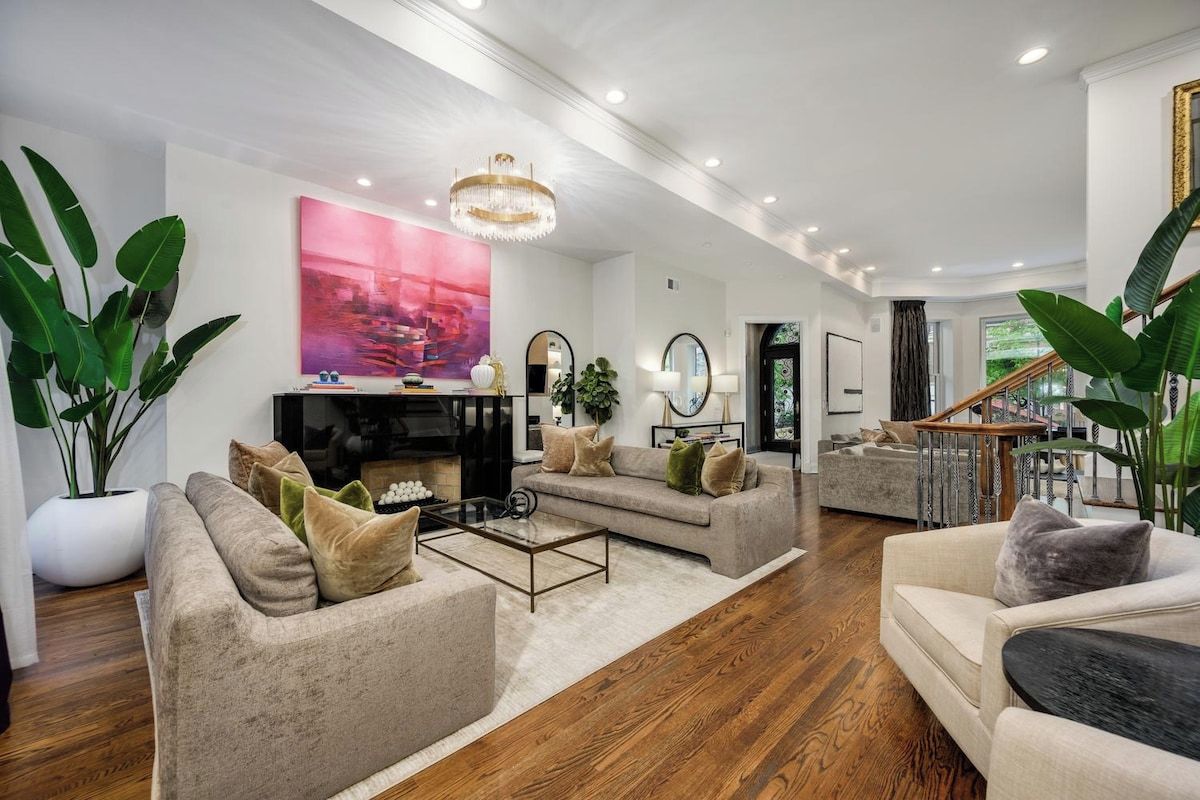 A spacious living room with a fireplace, a chandelier, and a staircase leading to an upper floor.