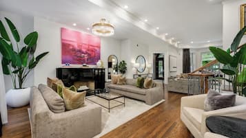 A spacious living room with a fireplace, a chandelier, and a staircase leading to an upper floor.