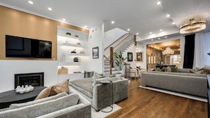 A modern living room with a fireplace, grey sofas, wooden flooring, and a staircase leading to another room.