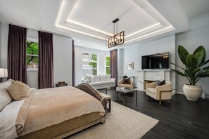 Quarto moderno com uma cama grande, área de estar com sofá e poltronas, televisão e lareira.