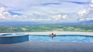 A man relaxing in a swimming pool with a scenic view of a green landscape and mountains in the distance. - Casita at Vista Del Paraiso-Incredable central valley view (Atenas)