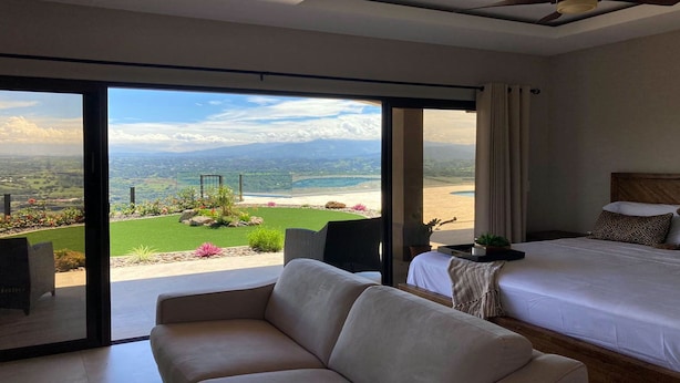 A bedroom with a large bed, a sofa, and a view of a landscaped garden and beach. - Casita at Vista Del Paraiso-Incredable central valley view (Atenas)
