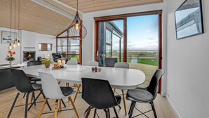 A modern dining area with a large table, black and white chairs, and a view of the sea through large windows. - Nice home in Sjølund with sauna (Sjølund)