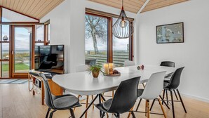 A modern dining area with a large table, chairs, a television, and a view of the outdoors. - Nice home in Sjølund with sauna (Sjølund)