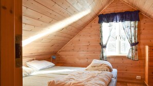 Ein gemütliches Schlafzimmer im Dachgeschoss mit schrägen Wänden, einem Bett mit Daunendecke, einem Nachttisch und einem Fenster mit Vorhängen.