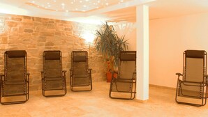 Ein Zimmer mit vier stuhlähnlichen Sitzgelegenheiten aus Metall, Mesh-Rückenlehnen und Sitzkissen, einer Steinwand, einem Blumentopf und einer Decke mit Einbaustrahlern.