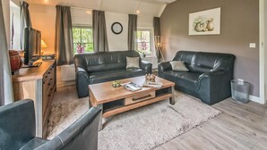 A modern living room with two black leather sofas, a wooden coffee table, and a small side table. There is a window with curtains, a clock on the wall, and a framed picture above the sofa. - Stunning home in Den Ham with WiFi (Den Ham)