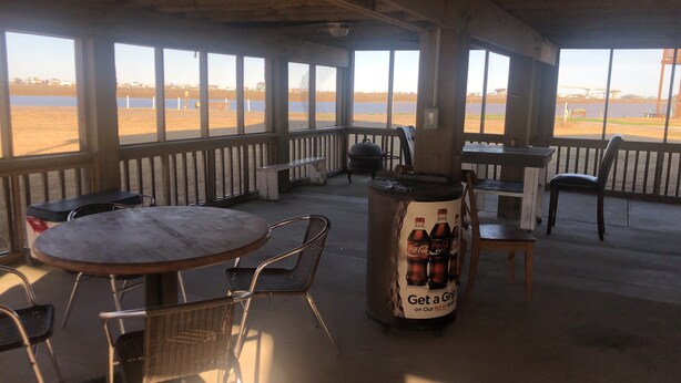 Eine Terrassengaststätte mit Tischen und Stühlen, einem großen Coca-Cola-Kühler und Blick auf den Strand.