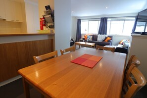 A dining area with a wooden table and chairs, a sofa with cushions, and a window with curtains.