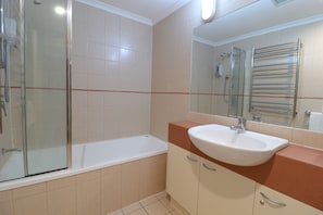 A modern bathroom with a glass-enclosed shower, a white bathtub, and a sink with a mirror above it.