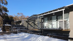 Un edificio moderno con balcón, una estructura de piedra y terreno cubierto de nieve.