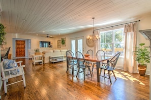 Un vaste salon doté d’un plancher en bois, un coin repas avec une table et des chaises en bois, un canapé blanc et un ventilateur de plafond.