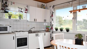Una cocina con armarios blancos, estufa, microondas y ventana con vista a follaje.