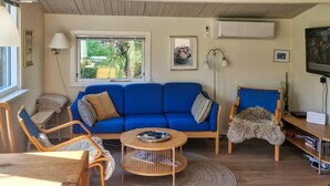 A living room with a blue sofa, wooden chairs, a small round table, and a TV. - 2 bedroom cozy home in Jægerspris (Jægerspris)
