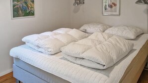 A bed with a quilted white duvet and pillows, a grey headboard, and a wooden floor. - 2 bedroom cozy home in Jægerspris (Jægerspris)