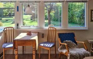 Una habitación con una mesa, dos sillas, un ventanal con vistas a un jardín y una lámpara colgante.