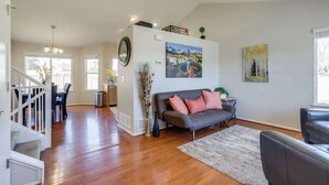 A spacious living room with hardwood floors, a grey sofa, a dining area with a table and chairs, and a staircase leading to another level. - 2 Master Suites with King beds fast Wifi (Centennial)