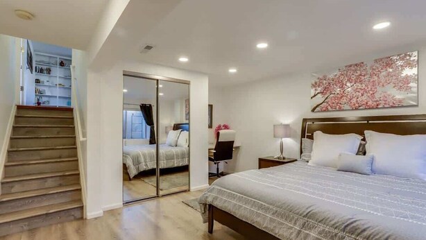 A bedroom with a large bed, a nightstand, a desk, a chair, a wardrobe, and a staircase leading to an upper level. - 2 Master Suites with King beds fast Wifi (Centennial)